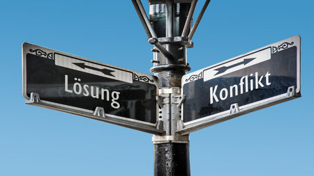 An image with a signpost pointing in two different directions in German. One direction points to conflict, the other points to resolution.の写真素材