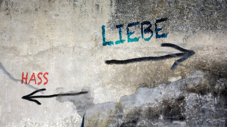 An image with a signpost pointing in two different directions in German. One direction points to love, the other points to hate.の写真素材