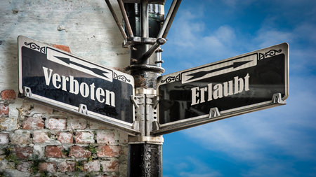 An image with a signpost pointing in two different directions in German. One direction points to Allowed, the other points to Prohibited.の写真素材
