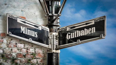 An image with a signpost pointing in two different directions in German. One direction points to Minus, the other points to Guthaben.の写真素材