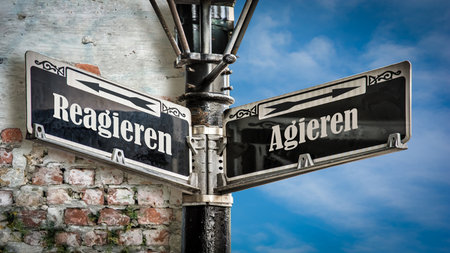 An image with a signpost pointing in two different directions in German. One direction points to act, the other points to react.の写真素材
