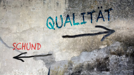 An image with a signpost pointing in two different directions in German. One direction points to quality, the other points to trash.の写真素材