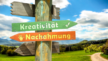 An image with a signpost pointing in two different directions in German. One direction points to creativity, the other points to imitation.の写真素材