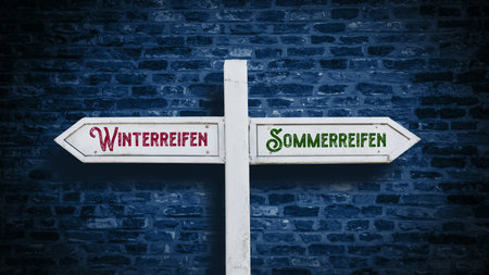 An image with a signpost pointing in two different directions in German. One direction points to summer tires, the other points to winter tires.の写真素材