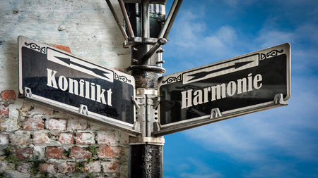 An image with a signpost pointing in two different directions in German. One direction points to harmony, the other points to conflict.の写真素材