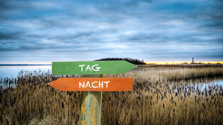 An image with a signpost pointing in two different directions in German. One direction shows day, the other shows night.の写真素材
