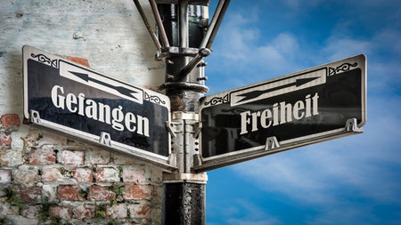 An image with a signpost pointing in two different directions in German. One direction points to freedom, the other points to captive.の写真素材