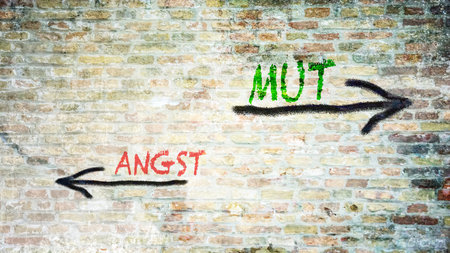 An image with a signpost pointing in two different directions in German. One direction points to courage, the other points to fear.の写真素材
