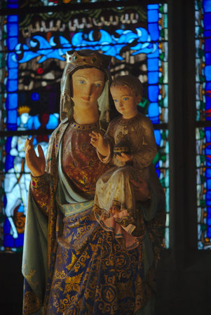 old statue of the virgin and the child, wooden, in the cathedral of clermont ferrand on stained glass backgroundのeditorial素材