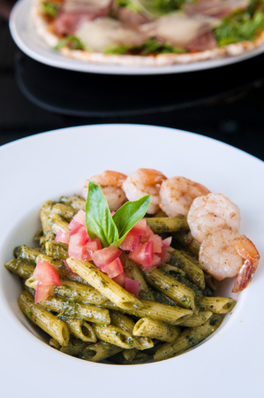 Penne Pasta with Pesto Sauce, shrimps tomato. Italian Cuisine on white plate, black tableの写真素材
