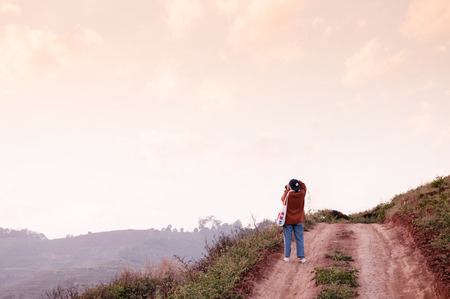 FEB 3, 2018 Chiang Mai, Thailand : Young woman taking photo of sunset sky on dirt path country road on the hill at evening in Chiang Maiのeditorial素材