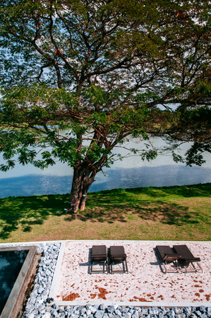 FEB 23, 2015 Kanchanaburi, Thailand : Resort style pool with vintage tiles, rocks, sand daybeds, big tree by the river shot from topのeditorial素材
