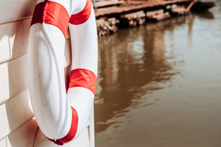 Close up shot of Red and white life buoy torus hanging on white wooden wall of river floating house or raft house with copy spaceの写真素材