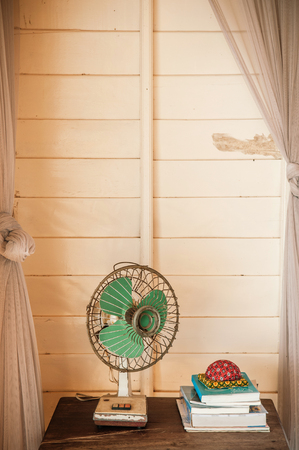 Retro vintage old design electric fan on wooden table in living room with a stack of books, warm daylightの写真素材