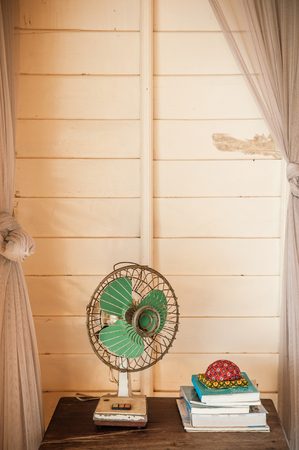 Retro vintage old design electric fan on wooden table in living room with a stack of books, warm daylight