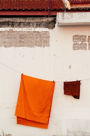 Yellow robe of Buddhist monk hanging on the old white concrete wallの写真素材