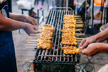 Grillled barbecue pork satay skewers on charcoal grill stove in street food market, Uthai thani - Thailandの写真素材