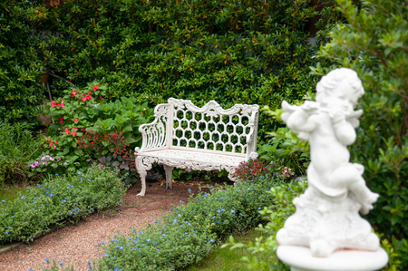 Vintage English country garden with flowers, white iron bench and cupid sculptureの写真素材