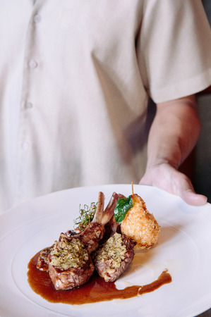 Waiter serving grilled lamb chops with crust, gravy and deep fried potato, close up shotの写真素材
