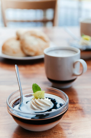 Delicious creamy vanilla caramel pudding with Kiwi in glass cup and coffee on wood tableの写真素材