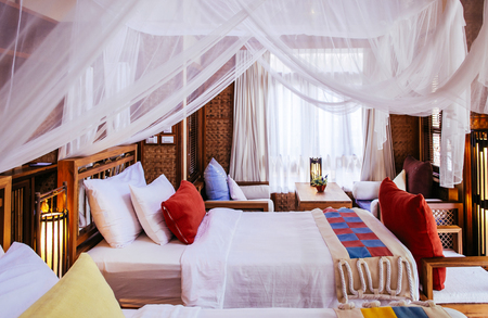 JUL 13,2013 Kanchanaburi, Thailand - Asian style Bedroom interior four poster bed with curtains and colourful fabric pillowsのeditorial素材