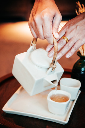 Close up shot of hands pouring hot chinese tea from teapot into a cupの写真素材
