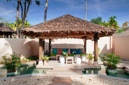 FEB 6, 2013 Phuket, Thailand - Vacation tropical resort thatched roof pavilion in water garden with clay house wall, colourful couch with pillows and ceramic stools and wood tableのeditorial素材
