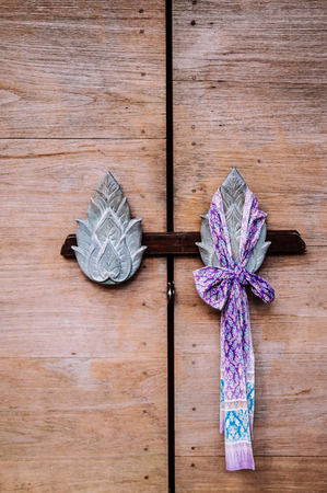 Old vintage wood door with Thai style lotus flower shape carved handles and beautiful fabric ribbonの写真素材