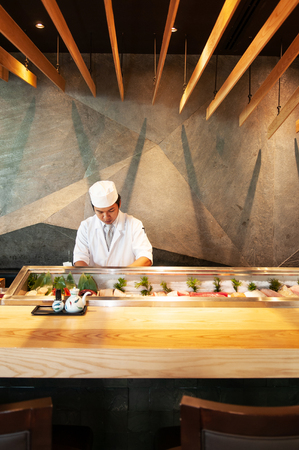 JUN 10, 2013 Bangkok, Thailand - Modern Vibrant Japanese Sushi bar interior, Wood decorated ceiling with warm lighting, Sushi chef working behind the barのeditorial素材