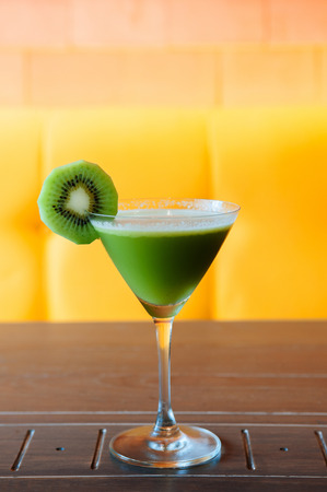 Sweet and sour kiwi smoothie in beautiful cocktail glass on wood table with bright yellow colour backgroundの写真素材