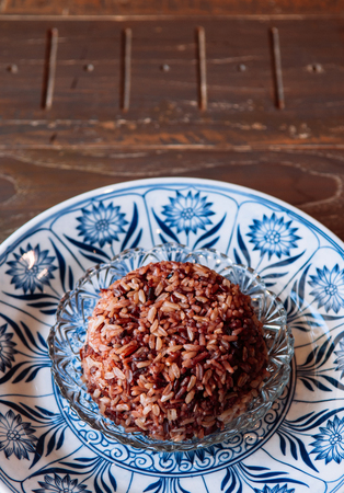 Thai rice berry steamed black rice in beautiful ceramic blue china plate - Top view shot on wooden tableの写真素材