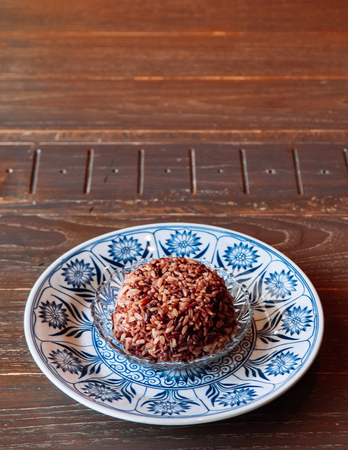 Thai rice berry steamed black rice in beautiful ceramic blue china plate - Top view shot on wooden tableの写真素材