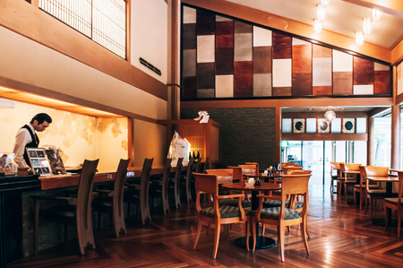 MAY 25, 2013 Gifu, JAPAN - Vintage Traditional Japanese dining room with wood tables and retro design chairs, old wood floor - warm light from ceiling lamp and restaurant staff working behind counter.のeditorial素材
