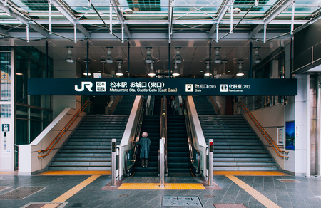 MAY 29, 2013 Nagano, Japan - Castle gate entrance with stairs, escalators and information sign of Matsumoto station with passengers back to camera. Cold colour tone imageのeditorial素材