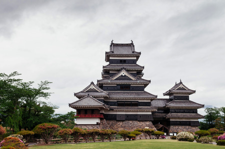 Matsumoto Castle Japan premier historic castle - Black crow castle - Nagano, Japan on cloudy day in summer with grass lawn and flower bushesのeditorial素材