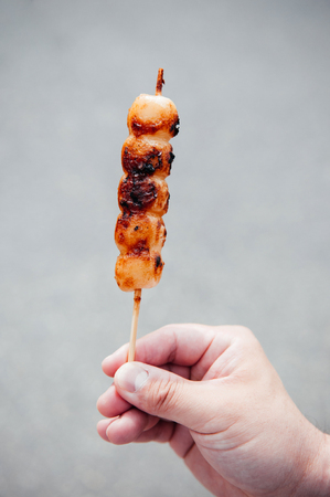 Japanese street food snack grilled Mitarashi Dango skewer with salty sweet sauce in handの写真素材