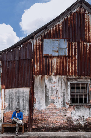 FEB 28, 2013 Songkhla, TAHILAND - Tourist sit on bench at vintage old grunge local house brick wall. Songkhla Nang Ngam street famous historic district in summer.のeditorial素材