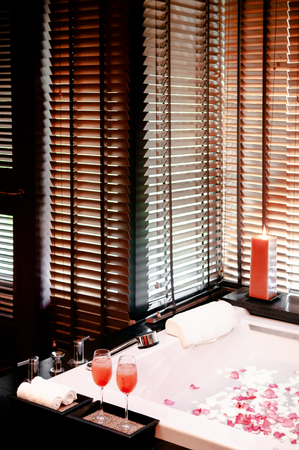 JAN 8, 2013 Bangkok, Thailand - Asian Thai spa rose flower bath with candle, and glass of Shirley Temple cocktail warm atmosphere with slightly natural light through bamboo venetian blindsの写真素材