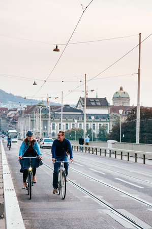 SEP 28, 2013 Bern, Switzerland - Swiss Couple riding bicycle on street of Bern city with old building and green dome of Swiss Parliament in backgroundのeditorial素材
