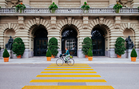 SEP 28, 2013 Bern, Switzerland - Local Swiss woman riding a bicycle pass front facade arch gates of Swiss Parliament building.のeditorial素材