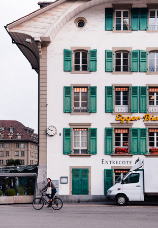 SEP 28, 2013 Bern, Switzerland - Local Swiss young woman riding a bicycle pass front of old Swiss style residential building with colourful windows in old town area.のeditorial素材