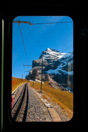 Jungfrau peak through train window on route from Kleine Scheidegg station climbing to Jungfraujoch pass grassfield and Swiss alps mountain rangeの素材 [FY310115244669]