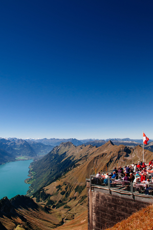 SEP 23, 2013 Entlebuch, Switzerland - Tourists at outdoor luch area on scenic terreace with Swiss flag of Mount Brienzer Rothorn with Lake Brienz and Swiss Alps viewのeditorial素材