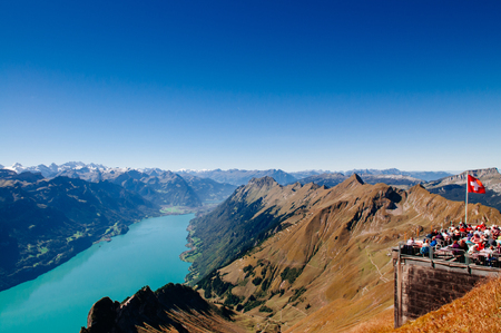 SEP 23, 2013 Entlebuch, Switzerland - Tourists at outdoor luch area on scenic terreace with Swiss flag of Mount Brienzer Rothorn with Lake Brienz and Swiss Alps viewのeditorial素材
