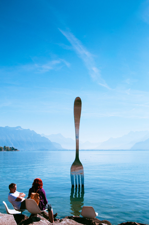 SEP 25, 2013 Montreux, Switzerland - Tourist at Lake Geneva shore with The Fork of Vevey modern installation art with Swiss alps view on bright sky day in autumnのeditorial素材