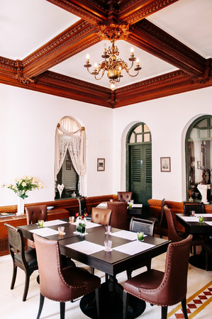 MAR 7, 2014 Bangkok, Thailand - Old vintage  house interior with black retro dinner tables, leather chairs, olive green wooden door and classic lamp on ceiling. Colonial building interiorのeditorial素材