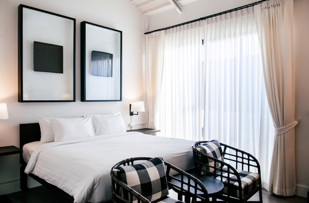 FEB 10, 2014 Chiang Mai, THAILAND - Asian contemporary hotel bedroom with wooden bed, white sheet, pillows, lamp, old wood table, retro rattan chairs and modern wall picture frameのeditorial素材
