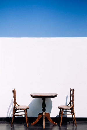 Vintage old wooden round dining table and chair at outdoor hard wood floor balcony, white wall with blue skyの写真素材