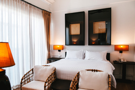 FEB 10, 2014 Chiang Mai, THAILAND - Asian contemporary vintage hotel bedroom with wooden bed, white sheet, pillows, lamp, old wood table, retro rattan chairs and modern wall picture frameのeditorial素材