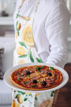 Thin crispy Italian Salami cheese black olives with marinara sauce pizza on white plate in waiter handの写真素材